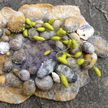 The image shows a small wall plaque created using Bergschaf fibres. The plaque is in the shape of a rock pool with seaweed.