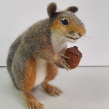 A needle felted grey squirrel holding an acorn